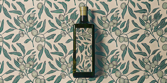 A bottle of early harvest extra virgin olive oil among fresh olive leaves.