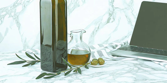 A bottle of polyphenol olive oil and olives next to a laptop used to research where to buy it.